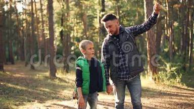 爱的爸爸在阳光明媚的秋日和儿子谈论大自然时站在森林里，做着手势，微笑着